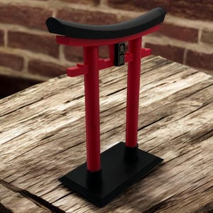 May include: A red and black miniature torii gate, a traditional Japanese gateway, with the text "MINI TORII" on the top beam. The gate is sitting on a wooden surface.