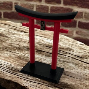 May include: A red and black miniature torii gate with a black base and a gold inscription that reads "鳥居".