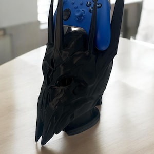 May include: A black plastic stand shaped like a skull with horns, holding a blue Xbox controller.