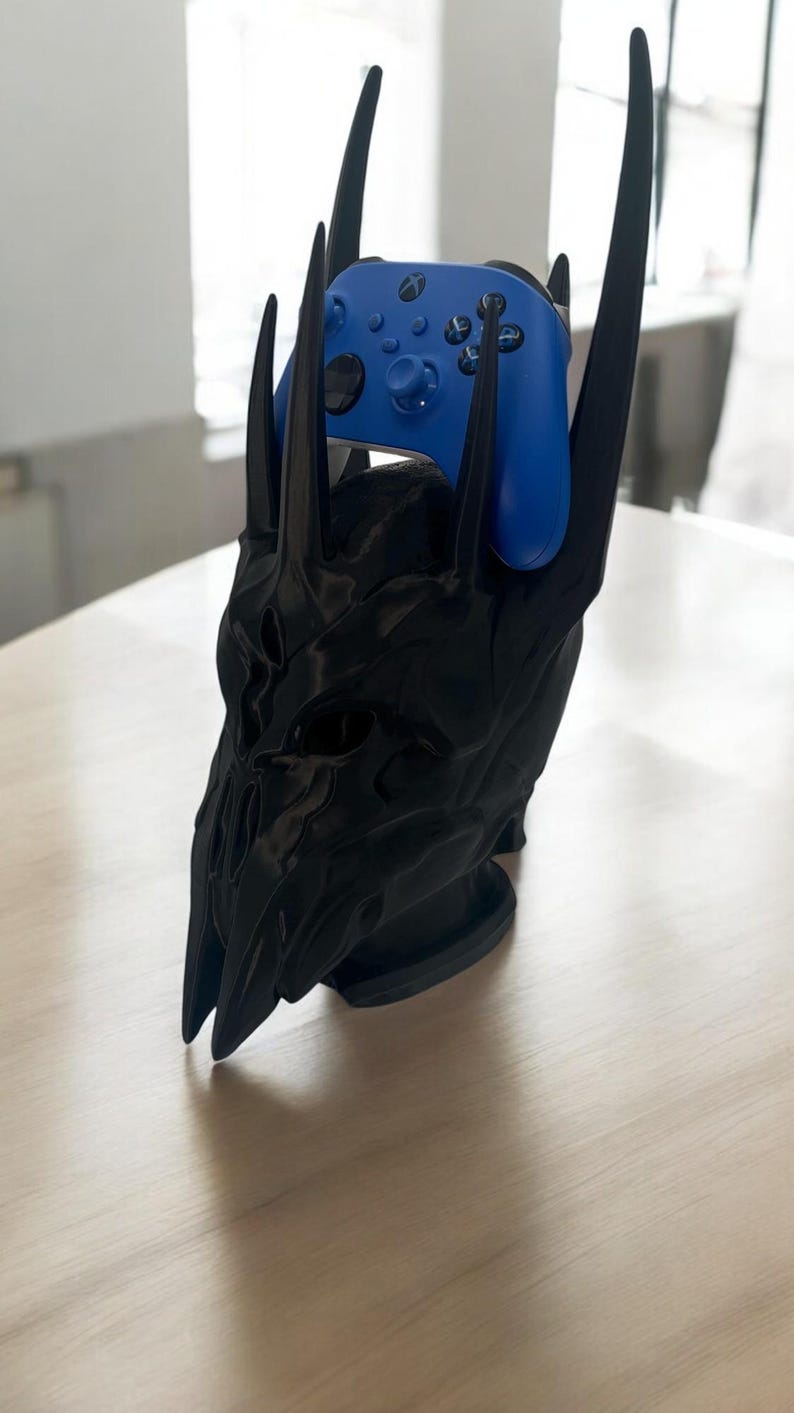 May include: A black plastic stand shaped like a skull with horns, holding a blue Xbox controller.