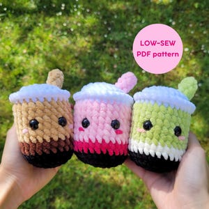 Peut inclure: Trois peluches de thé au boba crochetées en marron, rose et vert, chacune avec une base noire, des accents blancs et crème, et des yeux en boutons noirs. Le texte "LOW-SEW PDF pattern" est dans un cercle rose.
