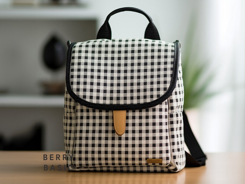May include: A black and white gingham patterned diaper bag with a black leather trim and a brown leather handle. The bag has a zipper closure and a small pocket on the front.