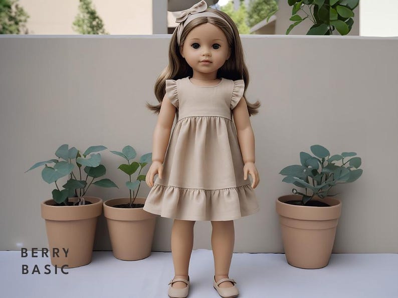 K&ouml;nnte beinhalten: Puppe in einem beigefarbenen Kleid mit R&uuml;schen&auml;rmeln und Saum, passendem Stirnband und beigen Schuhen. Die Puppe steht vor drei Topfpflanzen. Der Text "BERRY BASIC" befindet sich unten links im Bild.