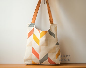May include: A tote bag with two orange shoulder straps featuring a cream-coloured base with a geometric pattern of orange, yellow, and grey parallelograms. The text BERRY BASIC is printed in the bottom right corner of the bag.