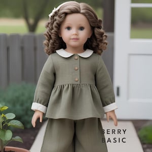 May include: A doll wearing a green collared dress with white trim and matching trousers. The doll has long brown curly hair and blue eyes.