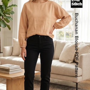 May include: A long-sleeved, light tan blouse with a round neckline and gathered cuffs, paired with solid black trousers. The image includes the text Ever Stitch Buchanan Blouse PDF Pattern, indicating a sewing pattern design for this garment.