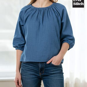 Può includere: Un top in denim blu con scollatura arricciata e maniche a tre quarti. Il top ha una vestibilità morbida ed è abbinato a jeans blu. Il logo Ever Stitch si trova nell'angolo in alto a destra.