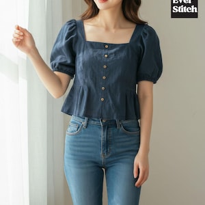May include: A navy blue blouse with a square neckline and short, puffed sleeves. The blouse features a row of buttons down the front and a peplum hem. The model is wearing blue jeans. The Ever Stitch logo is in the top right corner.