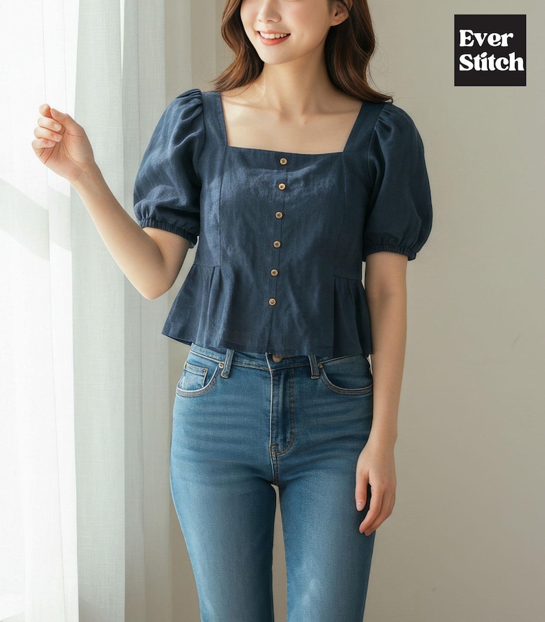Woman modeling a handmade navy square neck top with puff sleeves, a button-front, and a ruffled peplum hem, worn with jeans.