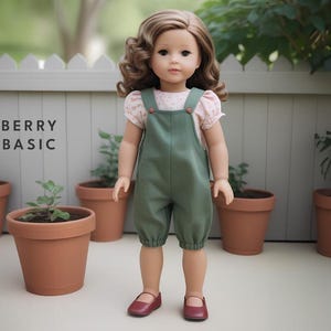 Könnte beinhalten: Eine Puppe trägt ein grünes Latzkleid mit einem Blusentop mit Blumenmuster. Die Puppe hat braunes Haar und blaue Augen. Die Puppe steht vor einem weißen Lattenzaun mit Topfpflanzen.