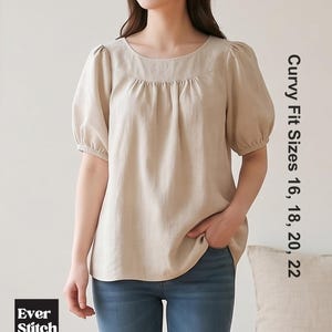 May include: A beige short-sleeved blouse with a round neckline and gathered puff sleeves. The garment features the text "Ever Stitch" and "Curvy Fit Sizes 16, 18, 20, 22" printed on the image. The blouse is paired with blue denim jeans.