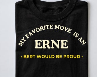 以下が含まれることがあります： MY FAVORITE MOVE IS AN ERNEというクリーム色の文字と、BERT WOULD BE PROUDという黄色の文字がプリントされた黒の半袖Tシャツ。クルーネックで、前面のグラフィックが見えるようにきれいに折りたたまれています。