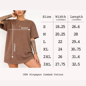 以下が含まれることがあります： 100%リングスパンコーマ綿を使用したブラウンの半袖Tシャツ。右側にはSから3XLまでのサイズ表があり、幅18.25〜27.75インチ、長さ26.6〜32.5インチの寸法がインチ単位で記載されています。