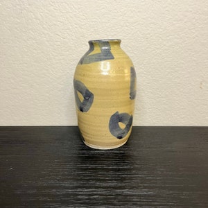 May include: A ceramic vase with a light brown glaze and blue abstract designs. The vase is about 6 inches tall and has a rounded body.