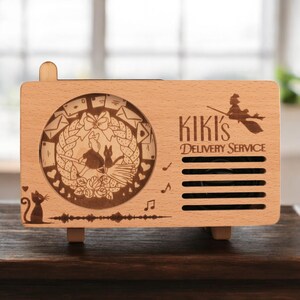 May include: A wooden music box with a laser-engraved design featuring Kiki's Delivery Service characters and the text "Kiki's Delivery Service".
