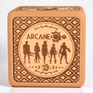 Könnte beinhalten: Eine Holzkiste mit hellbrauner Oberfläche. Die Vorderseite der Kiste zeigt ein kreisförmiges Design mit dem Wort "ARCANE" in einer stilisierten Schrift. Das Design enthält auch Silhouetten von sechs Figuren und ein Zahnrad-Symbol. Die Kiste ist mit einem sich wiederholenden Muster aus Blumen und geometrischen Formen verziert.