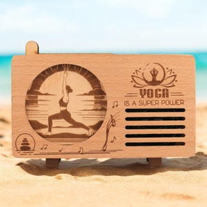 K&ouml;nnte beinhalten: Holzkiste mit einem Ausschnitt, der eine Frau zeigt, die Yoga vor einem Sonnenuntergang macht. Die Kiste tr&auml;gt die eingravierten Worte "Yoga is a super power".
