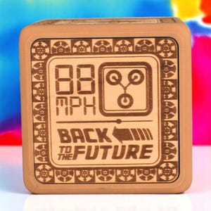 May include: A square, light brown wooden block with a laser-etched design inspired by "Back to the Future." The design includes the text "88 MPH," a graphic, and the words "BACK TO THE FUTURE."