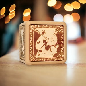 May include: A wooden box with a light brown finish and a silhouette of Alice falling down a rabbit hole. The box has a decorative border with floral designs.