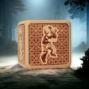 May include: A wooden box with a detailed geometric pattern and a laser-engraved image of a character holding a gun. The box is a light brown colour and has a slightly distressed look.