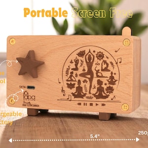 K&ouml;nnte beinhalten: Eine Holz-Musikbox mit einem Yoga-Motiv. Die Box ist 13,7 cm breit und 7,6 cm hoch. Sie verf&uuml;gt &uuml;ber einen Lautst&auml;rkeregler, einen Akku zum Aufladen und einen USB-Ladeanschluss. Die Box spielt Musik, wenn der Knopf gedreht wird.