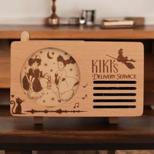 May include: A wooden music box with a laser-engraved image of Kiki and Jiji from Kiki's Delivery Service. The music box has a speaker grill and the text "Kiki's Delivery Service".