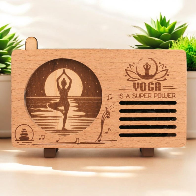 K&ouml;nnte beinhalten: Eine Holzkiste in Radioform mit einem lasergravierten Design. Das Design zeigt eine Silhouette einer Frau, die Yoga vor einem Mond und Wasser macht. Der Text "Yoga is a super power" ist ebenfalls auf die Kiste graviert.
