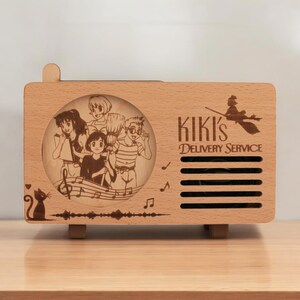 May include: A wooden music box with a laser-engraved image of characters from the movie Kiki's Delivery Service. The music box has a speaker grill and the text "Kiki's Delivery Service" is engraved on the front.