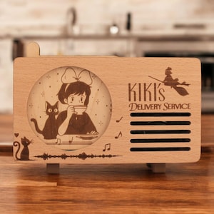 May include: A wooden music box shaped like a vintage radio with a laser-engraved image of Kiki from Kiki's Delivery Service, her cat Jiji, and the text "Kiki's Delivery Service".