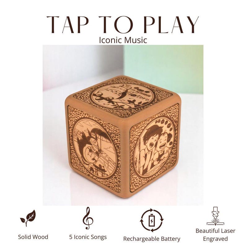 May include: A solid wood music box with laser-engraved illustrations. The cube-shaped box features iconic music and a rechargeable battery. The text "TAP TO PLAY Iconic Music" is at the top.