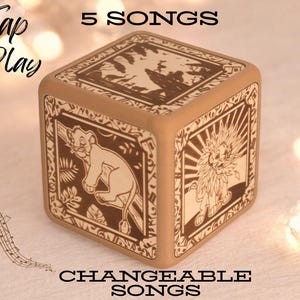 May include: A wooden cube music box with a Lion King theme. The cube has images of Simba and Mufasa on it. The text "Tap to Play" and "5 Songs" is printed on the box. The text "Changeable Songs" is printed below the box.