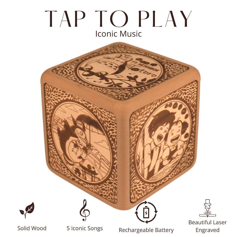 May include: A wooden cube music box with engraved illustrations from the movie "My Neighbor Totoro." The cube features the text "TAP TO PLAY" and "Iconic Music." It is made of solid wood and has a rechargeable battery.