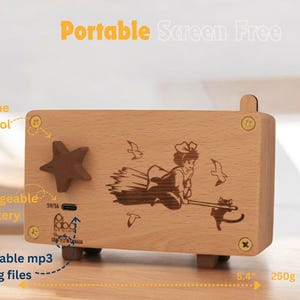 May include: A wooden music box with a laser-engraved image of a girl flying on a broomstick with a cat. The music box has a volume control knob, a rechargeable battery, and a slot for changeable mp3 song files. It measures 5.4 inches wide and 3 inches tall.