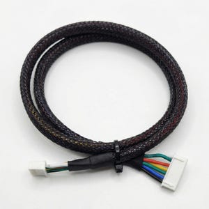 Pode incluir: Um cabo trançado preto e multicolorido com um conector branco em uma extremidade e um conector multicolorido na outra. O cabo é enrolado e preso com uma braçadeira preta. Os fios são vermelhos, amarelos, verdes, azuis e brancos.