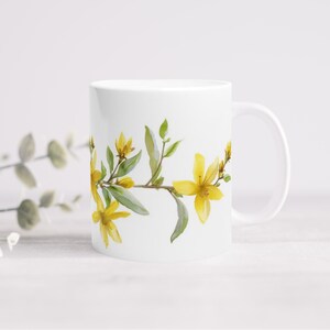 Könnte beinhalten: Weiße Keramiktasse mit einem Blumendesign mit gelben Blüten und grünen Blättern. Die Blüten sind in einer horizontalen Linie um die Tasse angeordnet.