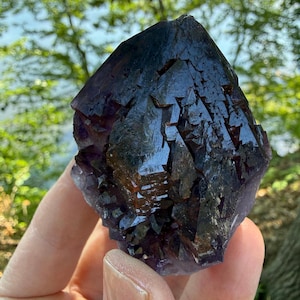 May include: A dark purple amethyst crystal cluster with a pointed, multifaceted structure. The mineral features deep violet hues, sharp geometric edges, and a glossy, reflective surface that catches light across its complex, jagged crystalline formation.
