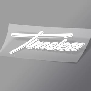 May include: White vinyl sticker with the word "Timeless" in a cursive font. The sticker is on a clear backing, with a gray background. The sticker has a shadow effect, giving it a 3D appearance.