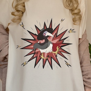 May include: A white t-shirt with a cartoon image of a bird wearing a mask and cape, surrounded by a red and yellow comic book style explosion.