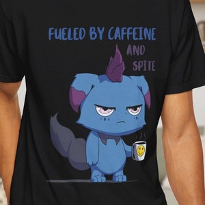 May include: Black t-shirt featuring a grumpy blue cartoon creature holding a coffee cup with a smiley face. The shirt has the text "Fueled by Caffeine and Spite" in blue lettering. The design is centered on the front of the shirt.