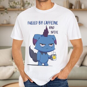 May include: White t-shirt with the text "FUELED BY CAFFEINE AND SPITE." The shirt features a cartoon illustration of a blue creature holding a coffee mug with a smiley face.