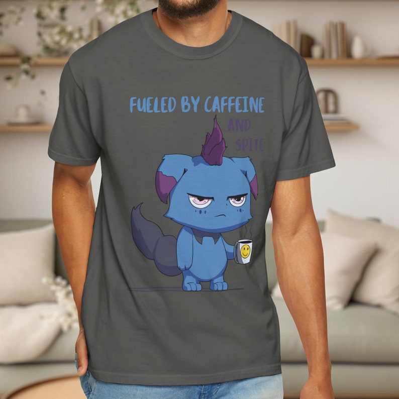 May include: Dark gray t-shirt with the text "Fueled by Caffeine and Spite." The shirt features a cartoon blue creature with a purple mohawk and ears, holding a coffee cup with a smiley face.