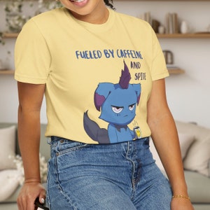 May include: Yellow t-shirt with the text "Fueled by Caffeine and Spite" above a blue cartoon creature holding a coffee cup with a smiley face. The creature has purple accents and a dark tail.