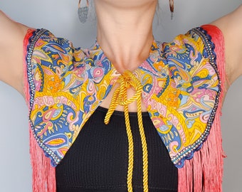 Blue, pink, and yellow retro fabric capelet with pink fringing, blue and silver trim, and gold cord fastening