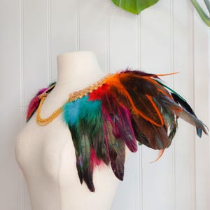 Collar de plumas multicolor con ribete decorativo dorado y cierre tipo collar.