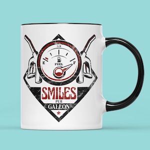 May include: White ceramic coffee mug with a black rim and handle. The mug features a black and white graphic of a fuel gauge with a red needle pointing to full. The text "Smiles Per Gallon" is printed below the gauge in black and red.