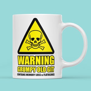 May include: White ceramic mug with a yellow warning sign featuring a skull and crossbones. The text reads "WARNING GRUMPY OLD GIT CONTAINS MEMORY LOSS & FLATULENCE".