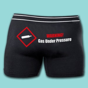 May include: Black boxer shorts with a white warning sign and the text "WARNING! Gas Under Pressure" printed on the back.