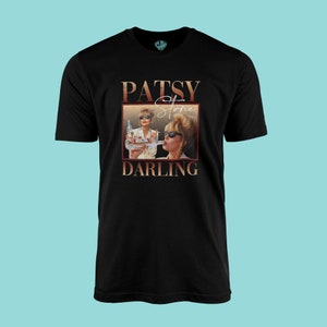 May include: Black t-shirt featuring a graphic of Patsy Stone from the show Absolutely Fabulous. The graphic shows Patsy Stone in a gold frame with the text "Patsy Stone Darling" in gold lettering.