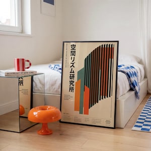May include: A framed vertical poster featuring a graphic design with vertical bars in orange, teal, and black on a cream background. The text includes Japanese characters and the English phrase Institute of Spatial Rhythm. The poster is displayed on a floor.