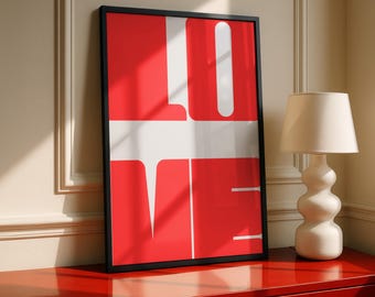 May include: A framed art print with the word "LOVE" in bold white letters against a red background. The artwork is in a black frame and rests on a red cabinet. A white lamp with a beige lampshade sits to the right.